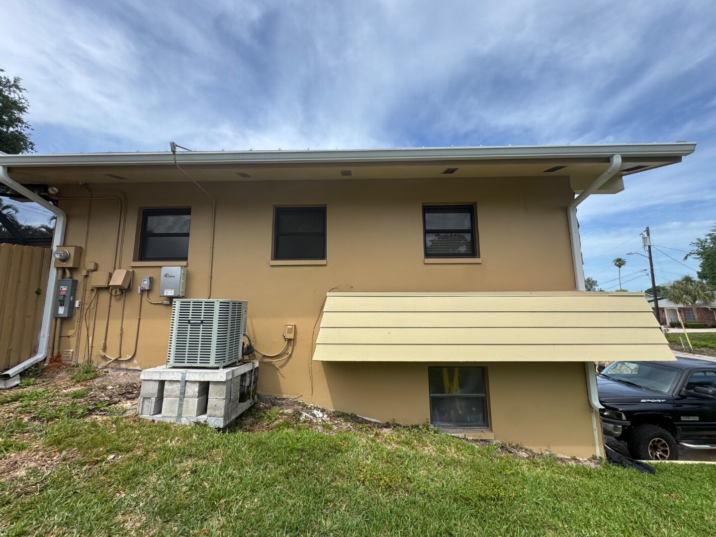 Dunedin home side wall before painting, tan stucco with yellow AC enclosure